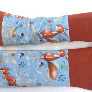 Puede incluir: Un par de calentadores de brazo azules y naranjas con un patrón de ardilla y hojas de otoño. Los calentadores tienen un puño marrón.