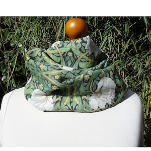 May include: A green and white floral patterned infinity scarf. The scarf displays a repeating pattern of white flowers and green leaves on a dark green background. The scarf is draped over a white mannequin.