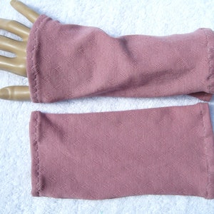 May include: A pair of pink arm warmers made of a textured fabric. The arm warmers are shown on a white surface.