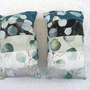 May include: Two rectangular cushion covers with a patchwork design featuring a green and white eucalyptus leaf pattern. The cushions have a teal blue border and gold accents.