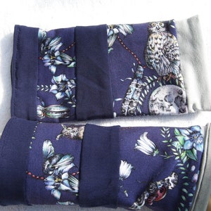May include: A pair of navy blue wrist warmers with a floral and owl print. The warmers are made of a soft, stretchy fabric and have a gray cuff.