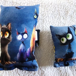 Könnte beinhalten: Zwei blaue dekorative Kissen mit Cartoon-Katzen. Das größere Kissen zeigt drei Katzen mit großen Augen auf einem dunkelblauen Hintergrund. Das kleinere Kissen zeigt eine einzelne Katze mit grünen Augen. Beide Kissen befinden sich auf einer weißen Oberfläche.