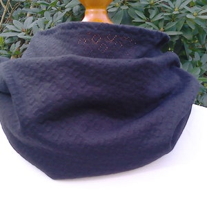 May include: A black knitted neck warmer with a textured pattern. The neck warmer is folded and displayed on a mannequin.