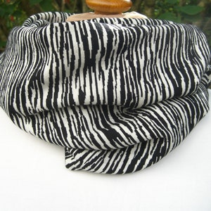 Könnte beinhalten: Ein schwarzer und weißer Rundschal mit vertikalem Streifenmuster. Der Schal ist gefaltet und drapiert, wodurch die Textur und das Design des Stoffes zur Geltung kommen. Der Schal ist aus einem weichen Material gefertigt.