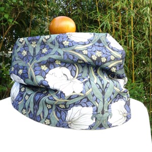 Op de afbeelding: Een blauwe en groene nekwarmer met een wit bloemenpatroon. Het patroon bevat gestileerde bladeren en bloemen.