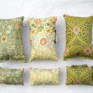 May include: Six decorative cushions with floral and geometric patterns in shades of green, yellow, and orange. The cushions are made of fabric and have a soft, quilted texture.