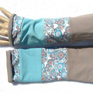 Könnte beinhalten: Ein Paar Armwärmer in Tealblau mit braunem Bündchen und einem weißen und tealfarbenen Paisley-Muster.