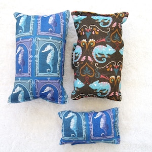 Könnte beinhalten: Drei dekorative Kissen mit verschiedenen Mustern. Das erste Kissen ist blau mit einem sich wiederholenden Muster von Seepferdchen in Rahmen. Das zweite Kissen ist braun mit einem sich wiederholenden Muster von Chamäleons und Herzen. Das dritte Kissen ist blau mit einem sich wiederholenden Muster von Seepferdchen in Rahmen.