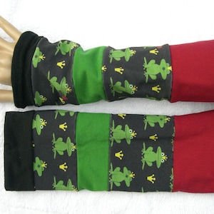 Puede incluir: Un par de calentadores de brazos negros, verdes y rojos con un patrón de rana y corona. Los calentadores de brazos están hechos de un tejido suave y elástico, perfectos para mantener los brazos calientes en climas fríos.