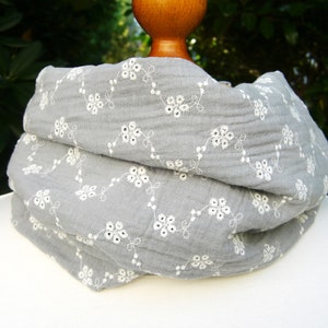 Może przedstawiać: Szary szal bawełniany z białym haftem kwiatowym.