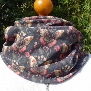 Op de afbeelding: Een zwarte nekwarmer met een bloemenpatroon met vlinders en roze bloemen.
