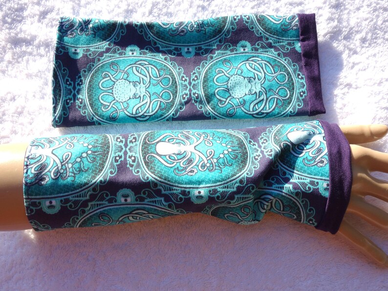 Puede incluir: Calentadores de brazo turquesa y morados con un dise&ntilde;o de pulpo. La tela presenta un patr&oacute;n ovalado con un pulpo en el centro, rodeado de adornos. Los pu&ntilde;os son de color morado liso.