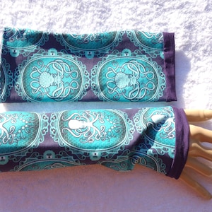 Puede incluir: Un par de guantes sin dedos y un art&iacute;culo rectangular a juego, ambos con un dise&ntilde;o de pulpo turquesa sobre un fondo morado oscuro. Los guantes tienen un pu&ntilde;o morado oscuro. El dise&ntilde;o del pulpo tiene forma ovalada con un borde decorativo.