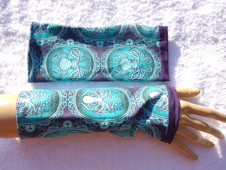 Puede incluir: Un par de guantes sin dedos y un art&iacute;culo rectangular a juego, ambos con un dise&ntilde;o de pulpo turquesa sobre un fondo morado oscuro. Los guantes tienen un pu&ntilde;o morado oscuro. El dise&ntilde;o del pulpo tiene forma ovalada con un borde decorativo.