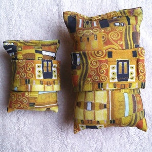 May include: Two small decorative cushions featuring a gold, brown and black geometric pattern. The design is reminiscent of Gustav Klimt's painting "The Kiss".
