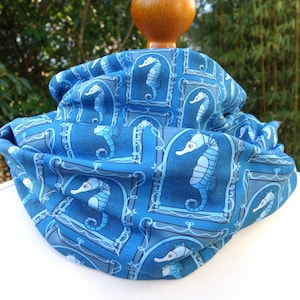May include: A blue fabric neck warmer with a repeating pattern of white seahorses in frames.