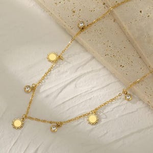 May include: A gold chain necklace with small sun charms and clear crystal accents.