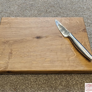 以下が含まれることがあります： 木製のまな板で、自然な木目があります。銀色のナイフが置かれています。