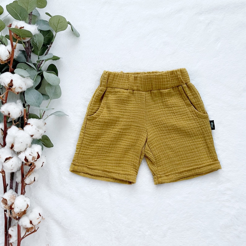 May include: Mustard yellow cotton shorts with a small black label. The shorts have two pockets and a wide waistband.