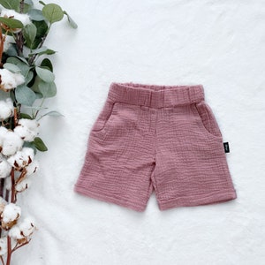 May include: A pair of pink cotton shorts with a textured weave. The shorts have two pockets and a waistband.