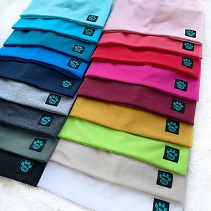 Peut inclure: Une pile de 14 bonnets en tricot colorés avec un logo en forme de patte. Les bonnets sont de différentes couleurs, notamment bleu, rouge, rose, vert et blanc.