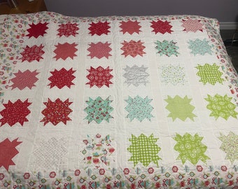 May include: A white quilt with a patchwork design featuring red, green and white stars. The quilt has a white background with a red, green and white border.