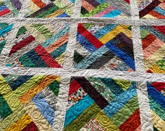 May include: A colourful patchwork quilt with a white background and a green border. The quilt is made up of squares of different fabrics, each with a different pattern. The squares are arranged in a diagonal pattern, creating a sense of movement. The quilt is quilted with a swirling pattern.