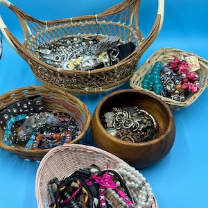 Può includere: Una collezione di braccialetti e collane colorati organizzati in quattro cesti diversi. I cesti sono fatti di vimini intrecciato e legno.