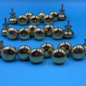 May include: A collection of 18 gold-toned round cabinet knobs with a shiny finish. The knobs have a screw-on design and are arranged in a curved pattern.