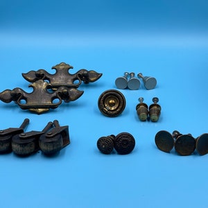 Peut inclure: Assortiment de quincaillerie d'armoire vintage en tons laiton et argent. Comprend des poignées de tiroir, des boutons et des roulettes de meubles.