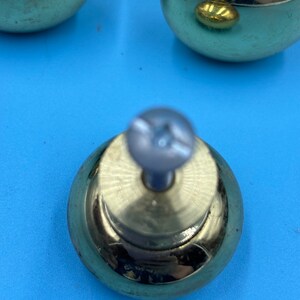 May include: A set of four gold-toned cabinet knobs with a round shape and a screw in the center. The knobs have a shiny, polished finish.