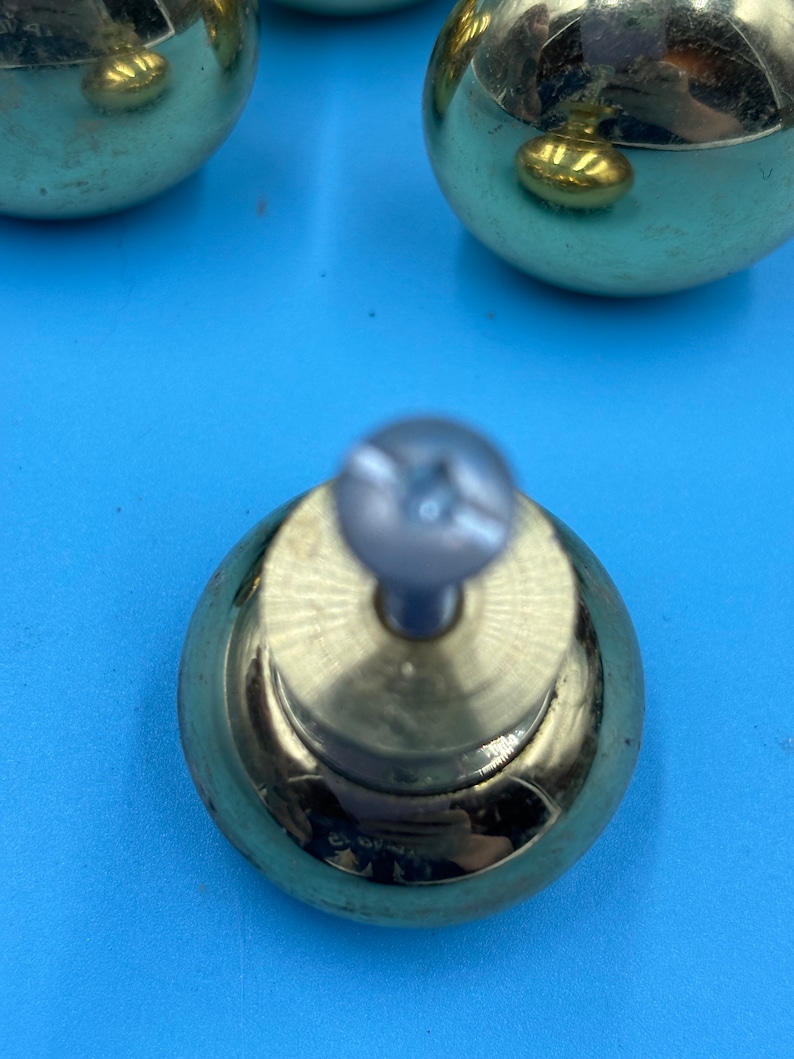 May include: A set of four gold-toned cabinet knobs with a round shape and a screw in the center. The knobs have a shiny, polished finish.