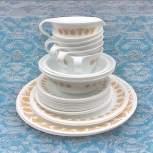 May include: A set of white Corelle dinnerware with a gold floral pattern. The set includes plates, bowls, and cups.