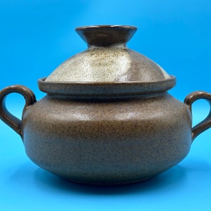 May include: A brown ceramic serving dish with a lid. The dish has two handles and a speckled brown glaze. The lid has a white glaze with brown speckles.