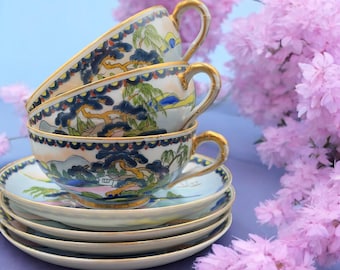 May include: A stack of four vintage teacups and saucers with a blue and gold floral pattern. The cups and saucers are stacked on a light blue surface with pink flowers in the background.