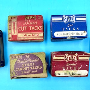 May include: Six boxes of assorted tacks, including blued cut tacks, cut tacks, double-pointed steel carpet tacks, and carpet tacks. The boxes are all made of cardboard and have a vintage look. The boxes are labeled with the brand name "STELCO" and the type of tacks.