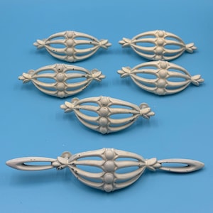 May include: Six white metal drawer pulls with a decorative, ornate design. The pulls have a cage-like design with rounded accents. One pull is longer than the others.