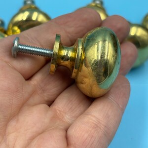 May include: A set of gold-toned cabinet knobs with a round, slightly domed shape. The knobs have a screw-on design and are made of metal.