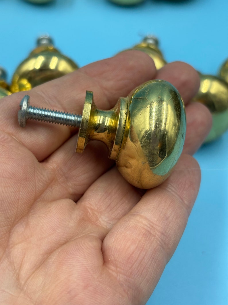 May include: A set of gold-toned cabinet knobs with a round, slightly domed shape. The knobs have a screw-on design and are made of metal.