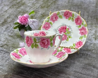 May include: A vintage teacup and saucer set with a pink rose floral pattern. The cup and saucer are white with a gold rim.