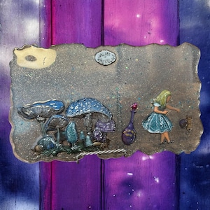 Puede incluir: Una pieza de arte rectangular de resina con el tema de Alicia en el País de las Maravillas. La obra de arte incluye ilustraciones detalladas de setas en tonos azules y morados, una botella y una figura de Alicia. El texto "Alice Wonderland" también está presente.
