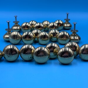 May include: A set of 18 gold-toned round cabinet knobs with a shiny finish. Each knob has a small screw for attaching to a cabinet door.
