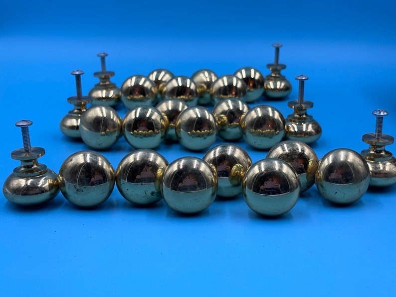 May include: A set of 18 gold-toned round cabinet knobs with a shiny finish. Each knob has a small screw for attaching to a cabinet door.