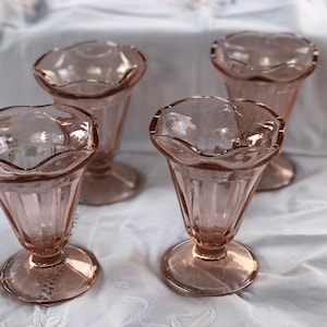 May include: Four pink glass ice cream dishes with a fluted design. The dishes have a scalloped rim and a pedestal base.