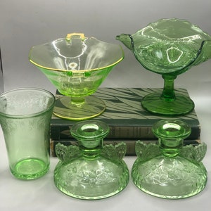 Op de afbeelding: Set van vijf vintage groene glazen stukken, waaronder twee kandelaars, een voetkom, een kleine kom en een drinkglas. Alle stukken hebben een bloemmotief.