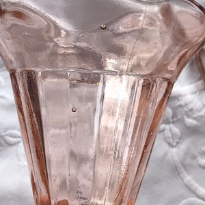 May include: A pink glass vase with a fluted design and a scalloped rim. The vase is made of clear glass with a pink tint.