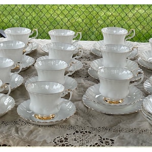 May include: A set of white teacups and saucers with gold trim. The cups and saucers have a delicate, scalloped edge. There is also a white bowl with a gold trim and scalloped edge.