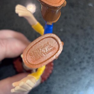 K&ouml;nnte beinhalten: Nahaufnahme einer Woody-Actionfigur aus der Toy Story-Reihe. Die Figur tr&auml;gt einen braunen Cowboy-Stiefel, einen gelben Hemds&auml;rmel und eine rote Weste. Der Fu&szlig; der Figur tr&auml;gt den Text "&copy;Disney/Pixar" und "Made in Vietnam".