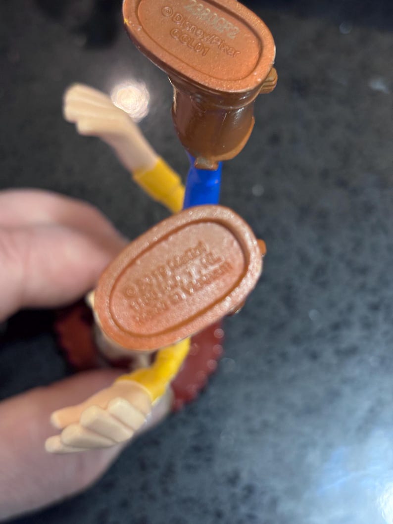 K&ouml;nnte beinhalten: Nahaufnahme einer Woody-Actionfigur aus der Toy Story-Reihe. Die Figur tr&auml;gt einen braunen Cowboy-Stiefel, einen gelben Hemds&auml;rmel und eine rote Weste. Der Fu&szlig; der Figur tr&auml;gt den Text "&copy;Disney/Pixar" und "Made in Vietnam".
