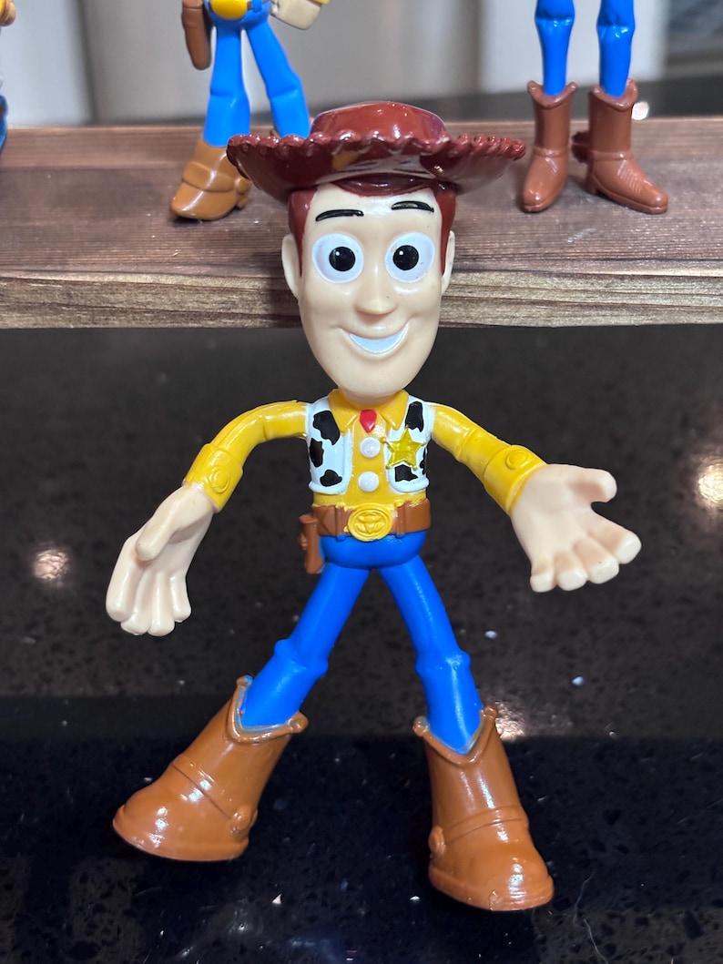 K&ouml;nnte beinhalten: Woody-Actionfigur mit braunem Cowboyhut, gelbem Hemd, blauer Hose und braunen Stiefeln. Die Figur hat ein Sheriff-Abzeichen und ein Holster. Das Spielzeug ist ein Sammlerst&uuml;ck aus der Toy Story-Reihe.